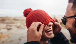 Žena se smije dok joj partner prekriva oči šeširom